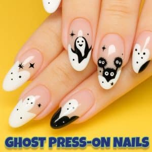 Square close-up photo of a hand wearing black-and-white ghost-themed press-on nails with spooky designs, including ghosts, stars, and crescent moons.